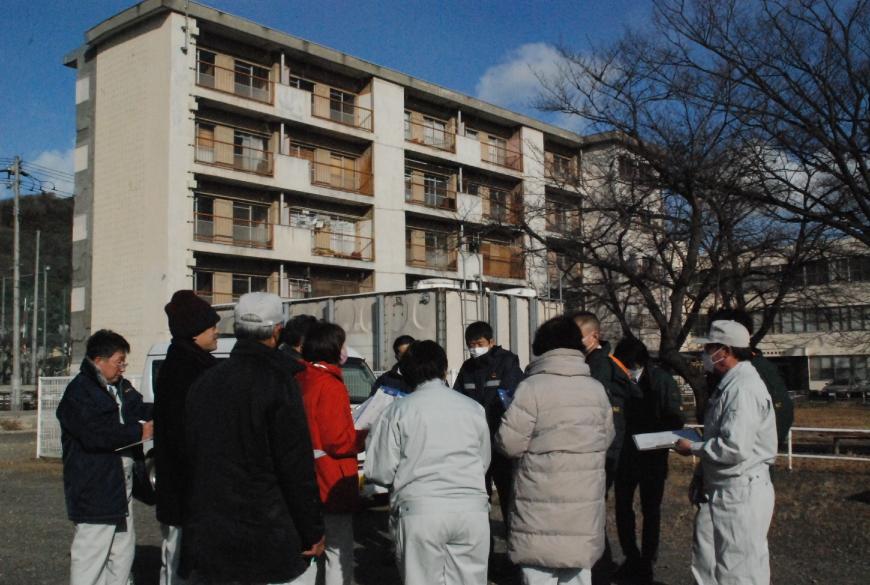 4階建ての市営住宅周辺で関係者が15名ほど集まっており、現地調査を行っている写真