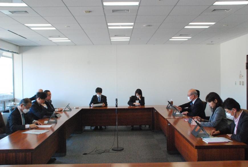 ロの字型の会議テーブルの席に関係者らが座り、経済民生常任委員会が行われている様子を後方席から見た写真