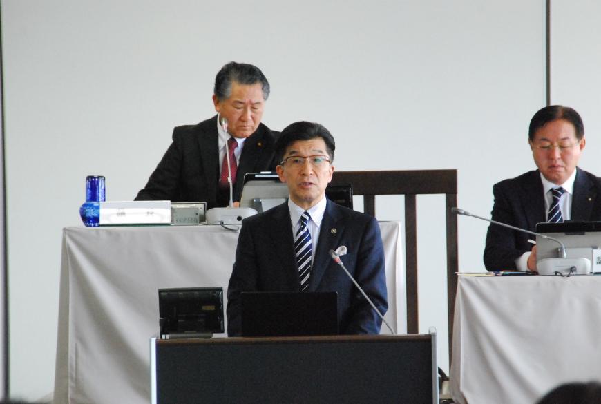 壇上に設置され卓上マイクに向かい話をしている市長の写真
