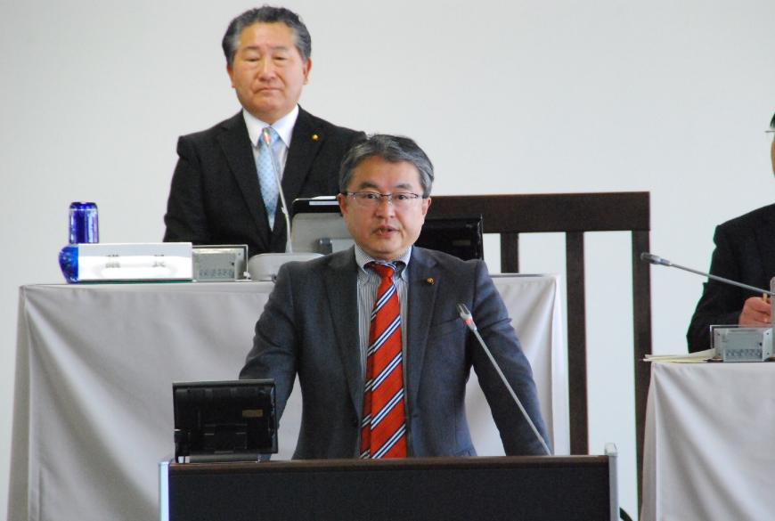 前方の壇上の卓上マイクに向かい話をしている川又康彦議員の写真