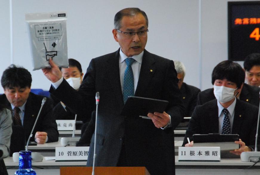 右手に非常用トイレのビニールパックを持ち卓上マイクに向かい話をしている後藤善次議員の写真