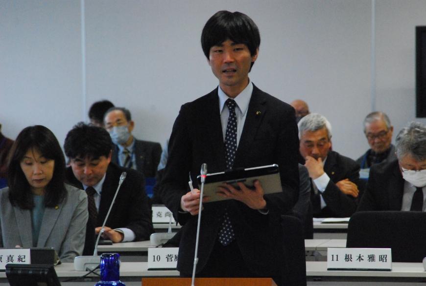 タブレットを持ち卓上マイクに向かい話をしている根本雅昭議員の写真