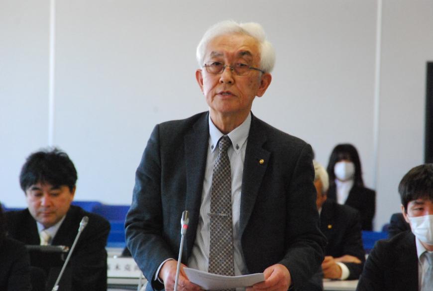 資料を手に持ち、卓上マイクに向かって話をする山田裕委員の写真