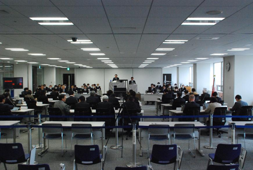 広い会議室で、50名ほどの関係者が席に座り、本会議を行っている写真