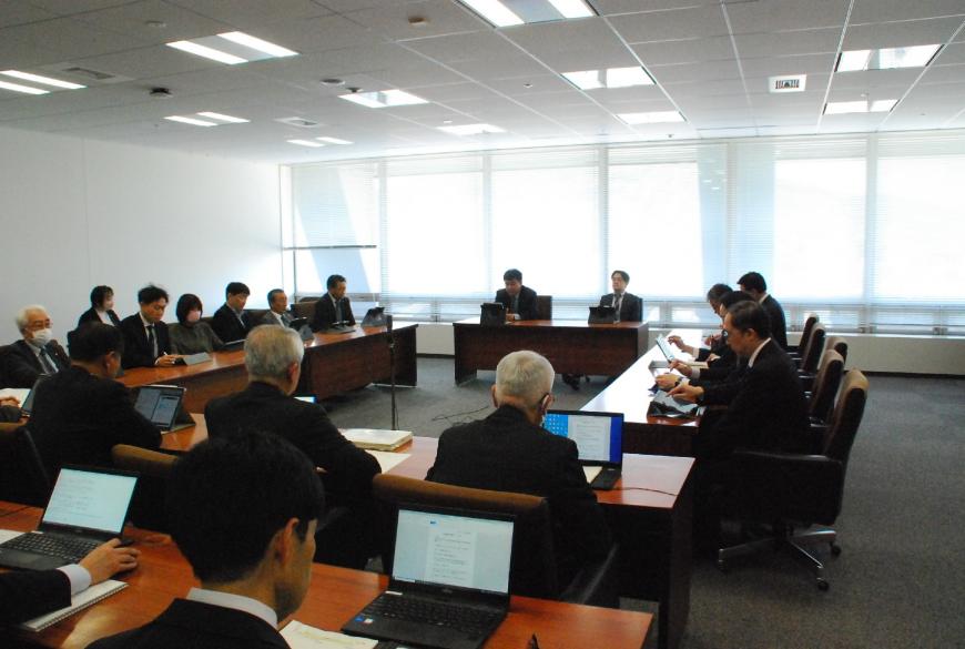 コの字型に配置された長机に13人が座り、その横に2列に並べられた長机に8人ほどが座り、タブレットの画面ノートパソコンの画面に映しだした資料を見たりしている写真