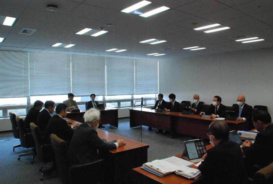 ロの字型に配置された長机に13人が座り、タブレットの画面を見ながら話し合いを行っている写真