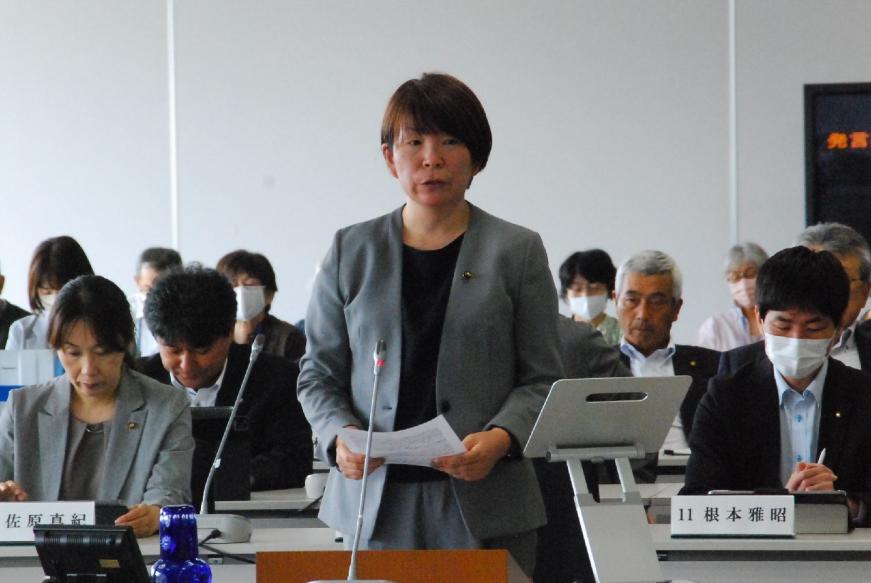 グレーのスーツを着た佐々木優議員が両手で資料を持ち登壇している写真