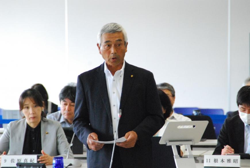 両手で資料を持った尾形武議員が登壇している写真