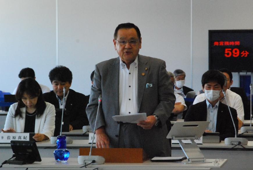 左手に資料を持った白川敏明議員が登壇している写真