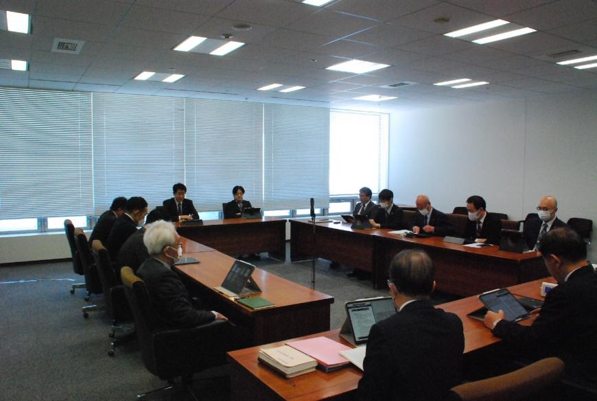 会議室でロの字型に配置されたテーブルに13人程が座りタブレットを見て協議をしている写真