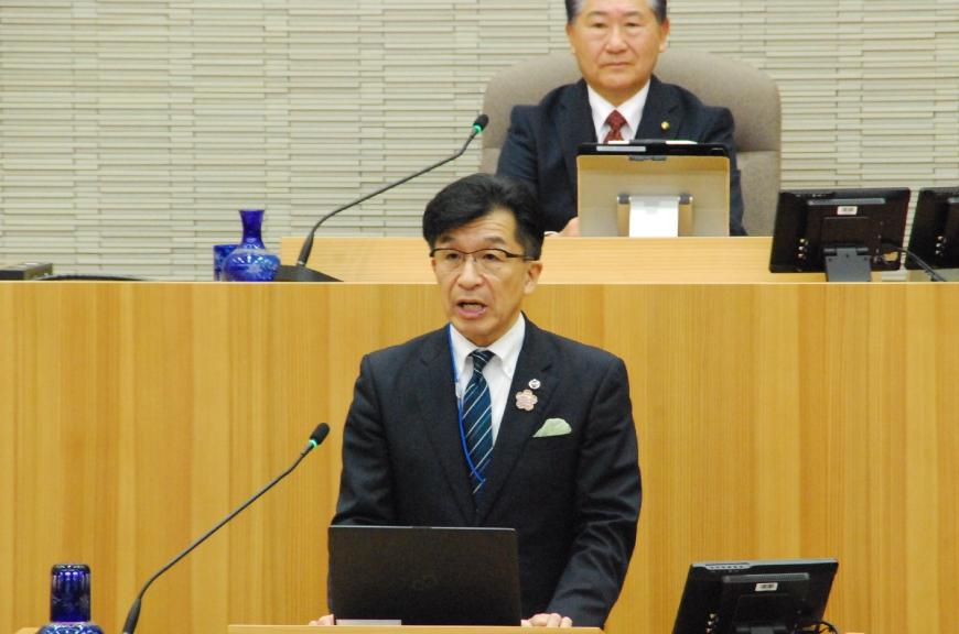 台の上にタブレットを置き真っすぐ前を向いて話をしている市長の写真