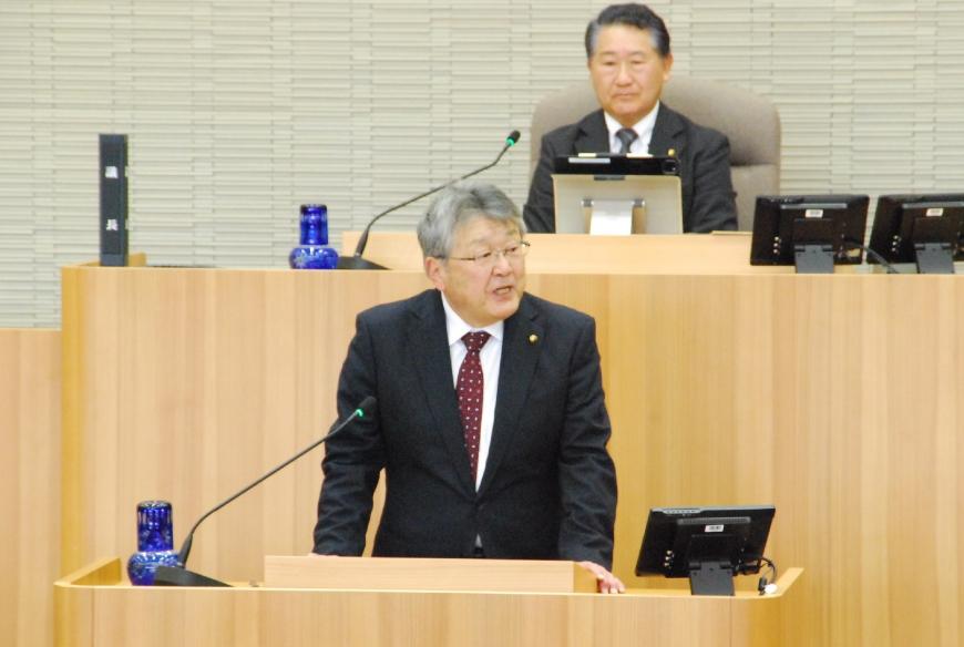 台の上に両手を置き左側を向いて話をしている鈴木正実議員の写真