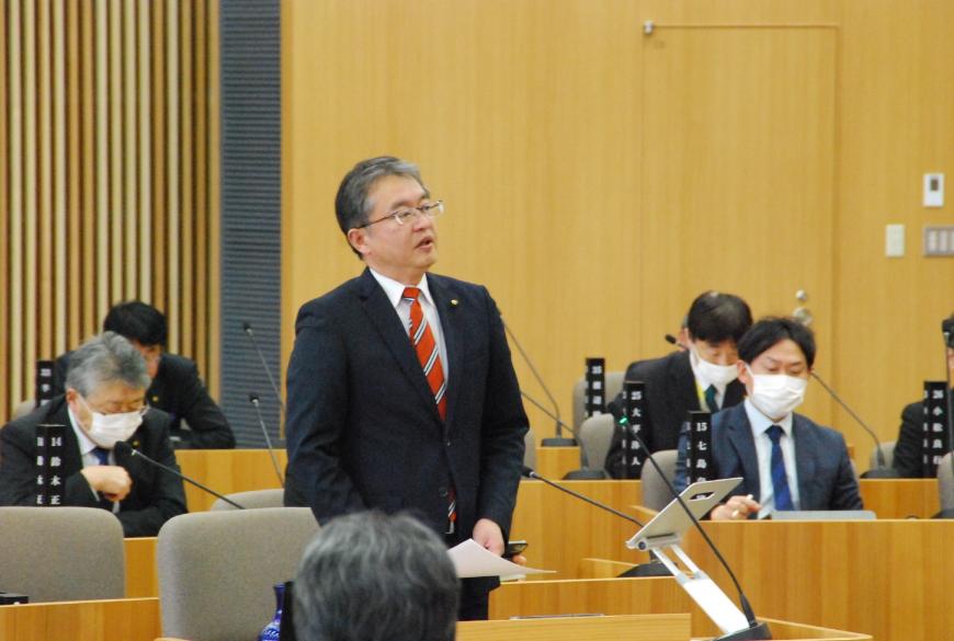 朱色と縞模様のネクタイをつけた川又康彦議員が話をしている写真