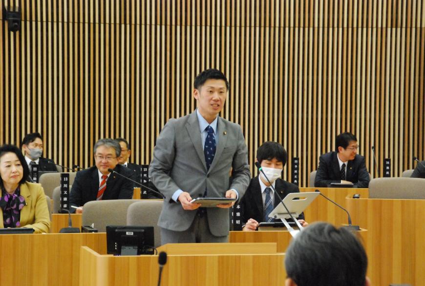 両手でタブレットを持ち前を真っすぐ向いて話をしている浦野洋太朗議員の写真