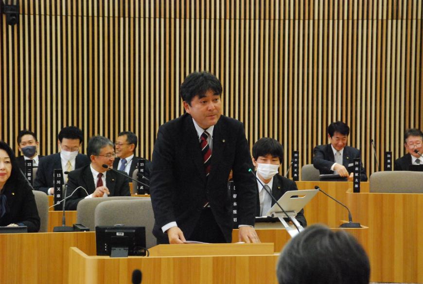 資料が置かれた台の上に両手を置き話をしている石原洋三郎議員の写真