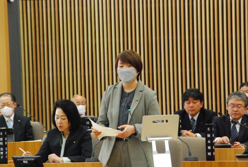 両手で資料を持ち真っすぐ前を向いて話をしているグレー色のジャケットを着た佐々木優委員の写真