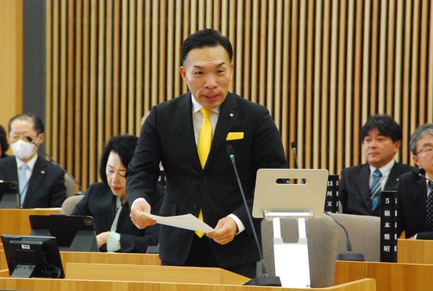 資料を両手に持った黄色のネクタイをつけた佐藤勢委員が話をしている写真