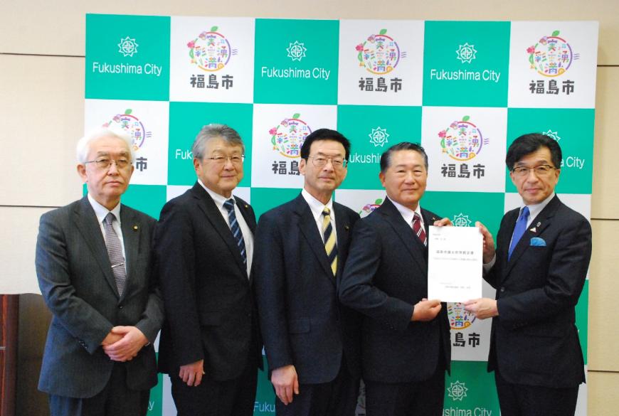 バックパネルの前で市長と代表の男性が書類を持ち、他3名の関係者が横一列に並んでいる写真