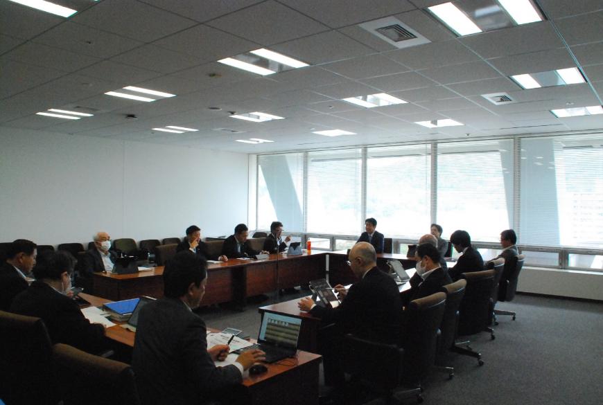 会議室でロの字型に配置された机に14人が座り、タブレットやノートパソコンの画面を見ている写真