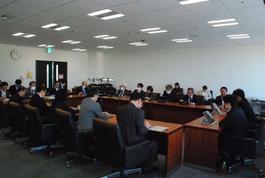 会議室でロの字型に配置された机に委員が座り、タブレットの画面を見ながら協議をしている写真