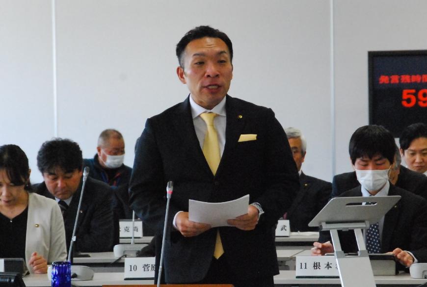 黄色のネクタイをつけた佐藤勢議員が資料を両手で持ち話をしている写真