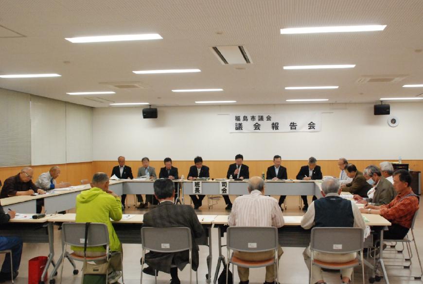 前方に設置された机と椅子に座る司会の方がマイクを持ち話し、その様子を参加された方々が聞いている写真