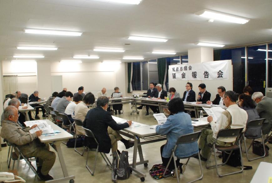 ホワイトボードに「福島議会 議会報告会」の横断幕が設置され、ロの字型に設置された机と椅子に参加者が座り資料を手に取り説明会の話を聞いている様子の写真