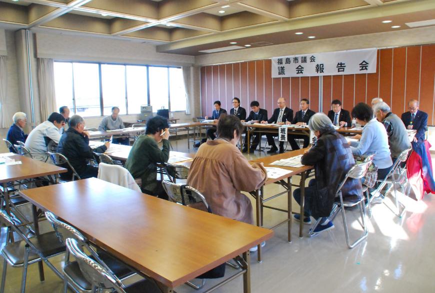 福島市議会議会報告会と書かれた横断幕が前方に掲示され、ロの字型に設置された机の前方に関係者の方々が座り、参加者の方々が会場内の席に着き、意見交換会が行われている様子の写真