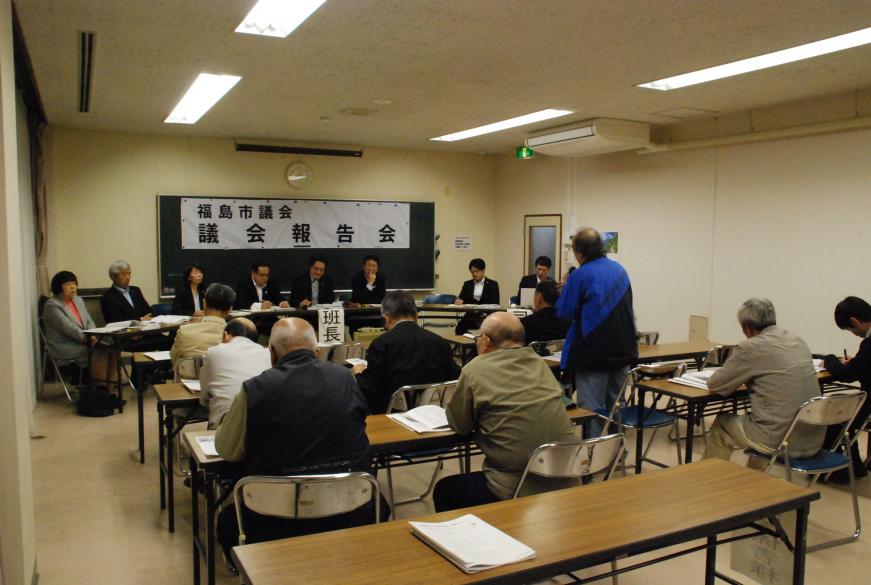 福島市議会 議会報告会にて参加された1名の男性が立ち、前方に座る方々に向けて話をしている様子の写真