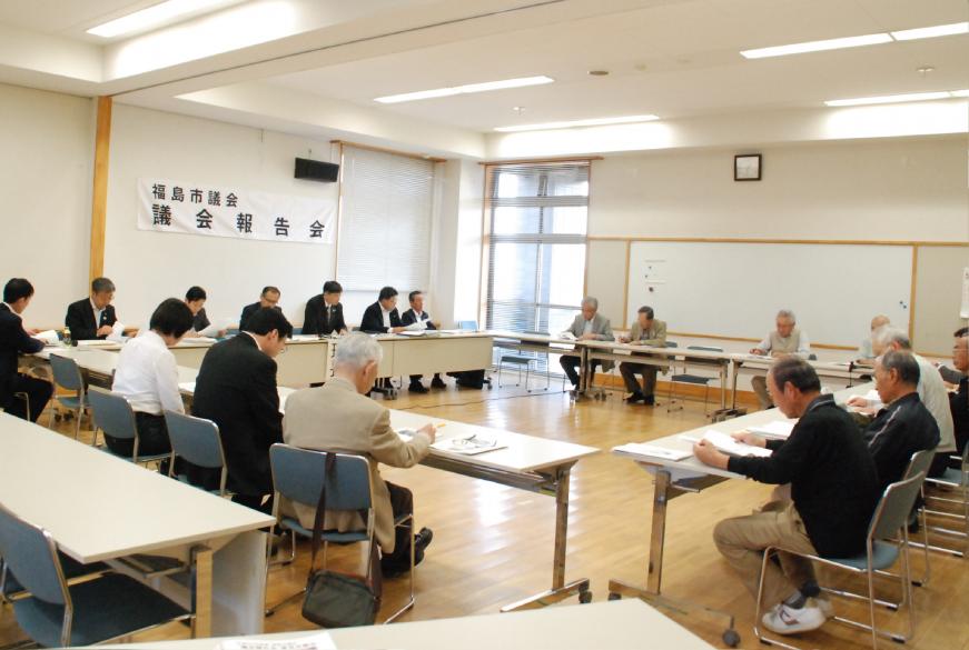 福島市議会 議会報告会に参加された方々が、室内に設置されたロの字型に配置されたテーブルと椅子に座り手元の資料に目を通している様子の写真