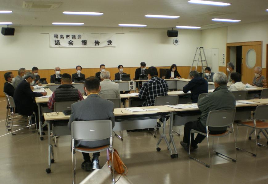 福島市議会議会報告会と書かれた横断幕が前方に掲示され、ロの字方に設置された机の前方に関係者の方々が座り、参加者の方々が会場内の席に着き、意見交換会が行われている様子の写真