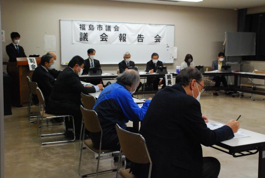 前方の白版に福島市議会議会報告会と掲示され、関係者の方々と参加者の方々がコの字に設置された机の席に着き、資料に目を通しながら会議が行われている様子の写真