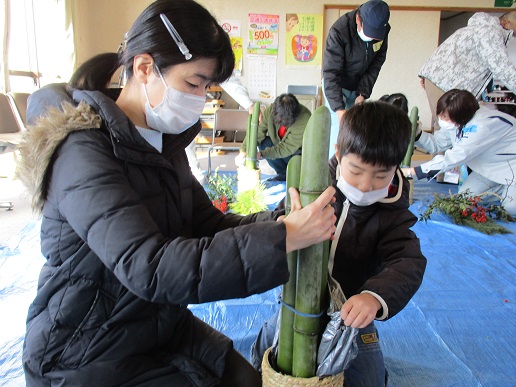 缶に立てた竹を女性が支え、男の子が缶の中に袋から砂を入れている写真