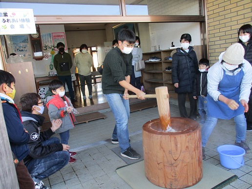 小さな男の子や他の参加者が見守る中、杵を振り下ろした男性の写真