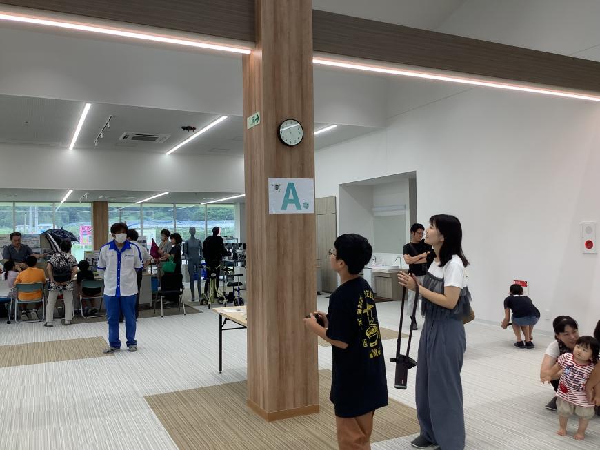「A」と書かれた紙が貼られた柱のある室内で、男の子がドローンを操作している写真