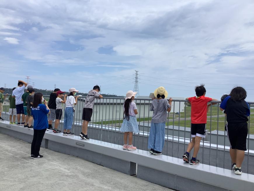 参加している子供たちが、建物屋上のフェンス部分に横一列にに並び、屋上からの景色を見ている様子の写真