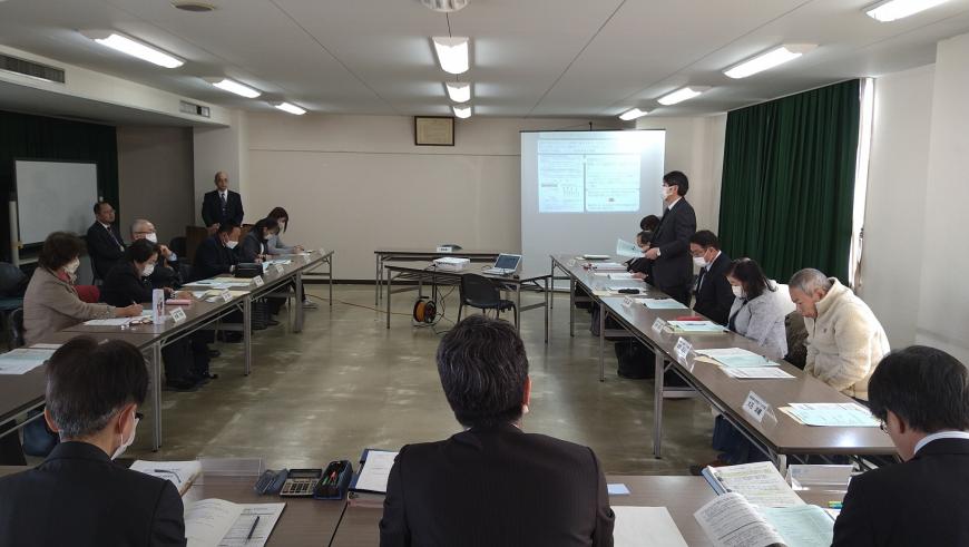 会議室前方のモニターに資料が映され、コの字型に配置されたテーブルと椅子に座り話をしている議会の様子の写真