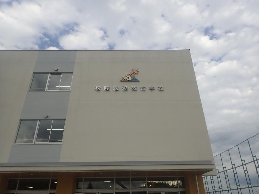 松陵義務教育学校の文字の上に公章がある建物外観を下から撮影した写真