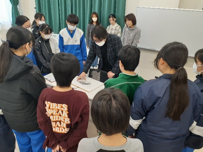 説明する男性講師の周りに集まり話を聞いている参加者達の写真
