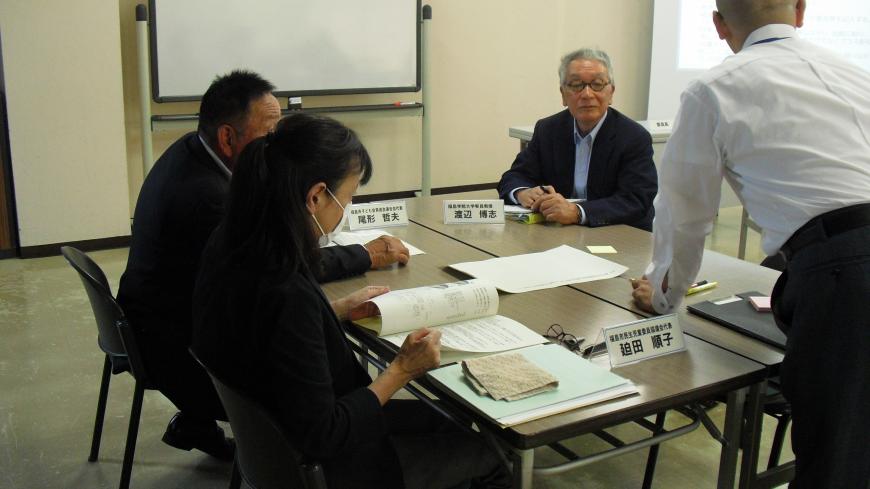 テーブルと椅子が設置され、ネームプレートの置かれた場所に参加者が着席した会議の様子の写真