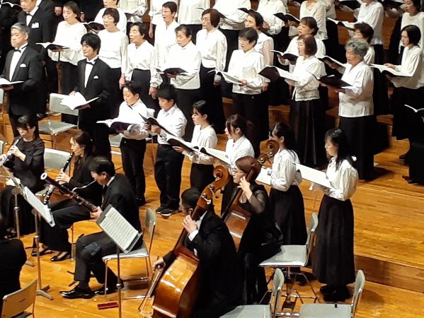 白と黒の衣装を着た合唱団と演奏者が歌や演奏を披露しているアップ写真