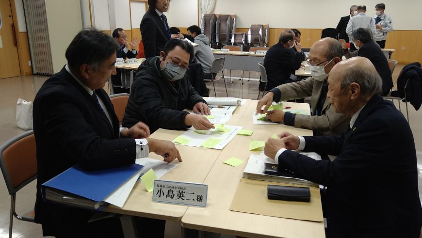 小島英二様と書かれたテーブル席に4人が着席し会議が行われている写真
