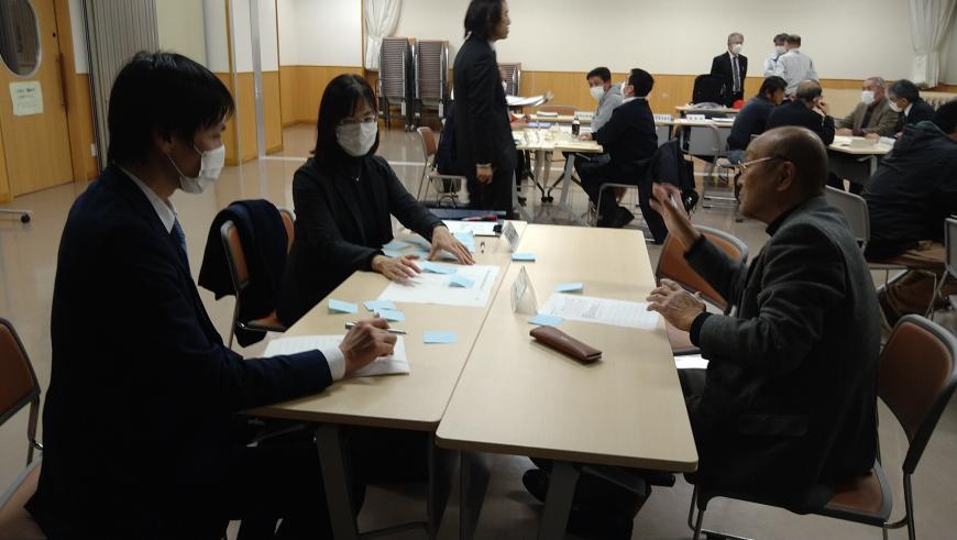 男性が話をするのを聞いている男性と女性の会議の様子の写真