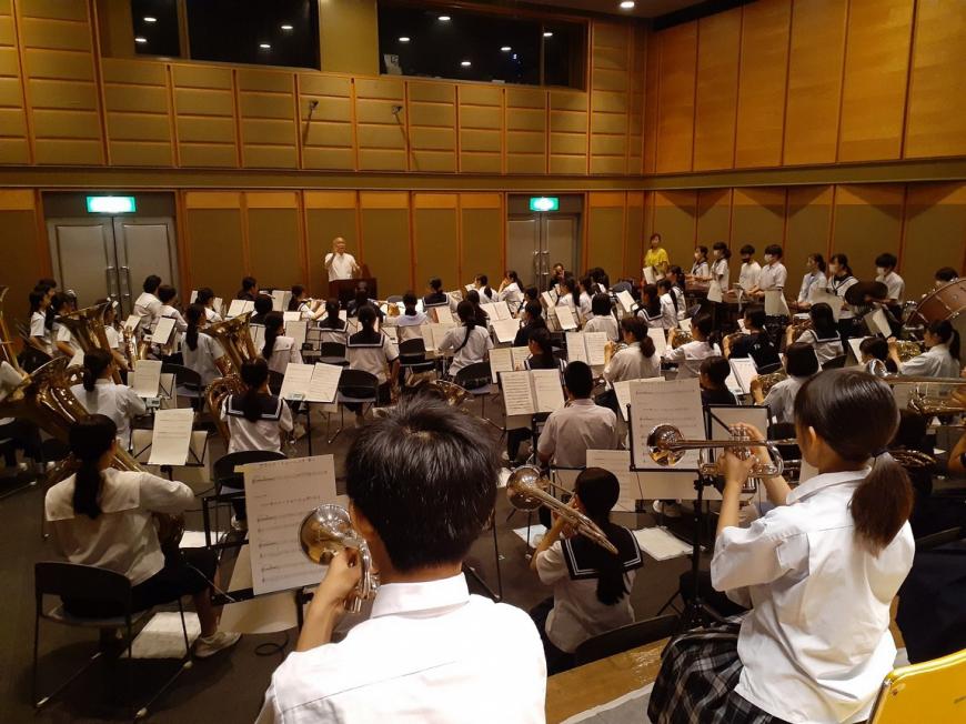 制服を着た学生達が7つのパートに分かれて演奏の練習をしている全体の写真