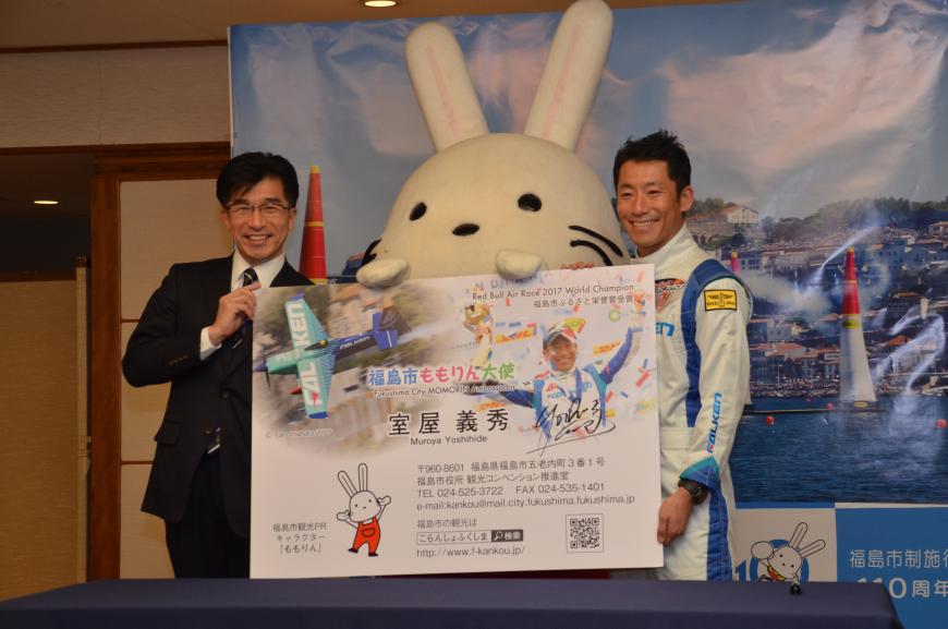 ももりん大使の名刺の大きな見本を市長とももりん、室屋義秀氏が一緒に持ち笑顔で写っている「福島市ももりん大使」のPR用名刺贈呈式の様子の写真