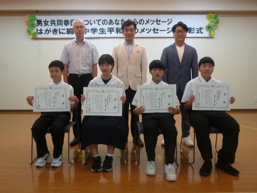 前列にメッセージ部門入賞者の生徒4名が賞状を持って椅子に座り、後方に市長と関係者の方2名が並び写っている記念写真