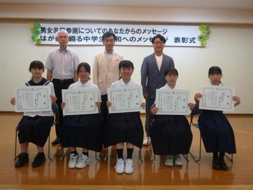前列にイラスト部門入賞者の生徒5名が賞状を持って椅子に座り、後方に市長と関係者の方2名が並び写っている記念写真