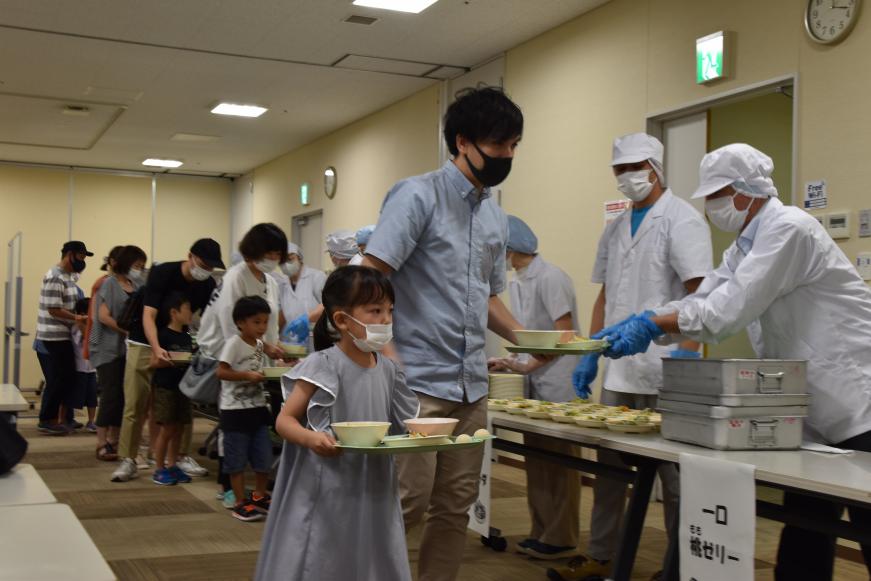 沢山の親子が列になり並び、職員の方々が配膳し、それを受け取る様子を写した写真