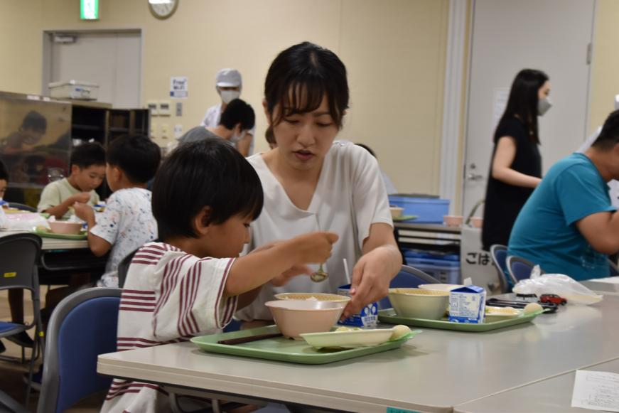 お母さんが皿に手を添え、子どもがカレーを食べている様子の写真