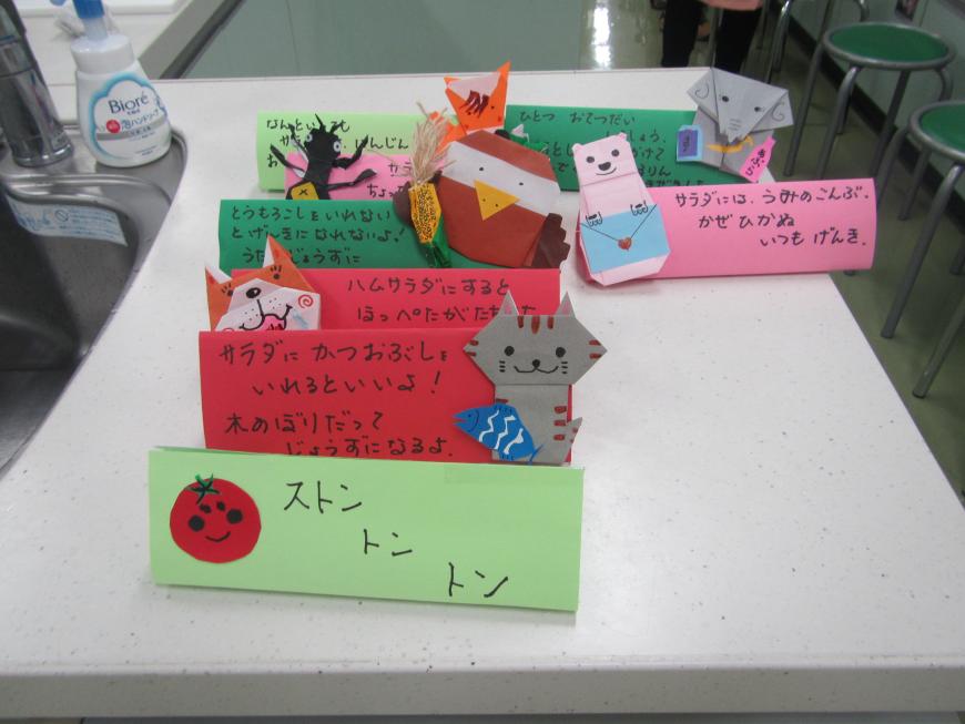 折り紙で作られた動物達が貼られ、赤、ピンク、緑の紙に文章が書かれた台紙が並んだ写真